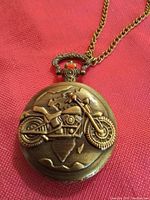 Close-up photo of the pocket watch front cover showing embossed motorcycle design and chain attachment.