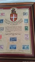 Close-up of framed Newfoundland stamp collection showing coat of arms, text, and several vintage stamps on beige background