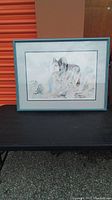 Full frontal image of framed watercolor style print depicting a wolf in natural setting, resting on a black surface.