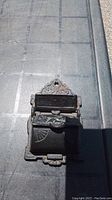 Front view of vintage black cast iron match safe showing hinged lid and embossed patterns on surface.