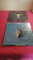 Two vintage Eagles records placed side by side on a red surface, showing fronts of album covers with some age wear visible