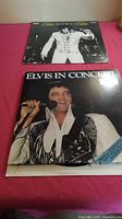 Two vintage Elvis Presley vinyl LP records stacked on a red surface showing the front covers of the albums.
