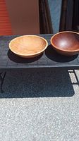 Two vintage wooden mixing bowls placed outdoors on a dark surface under sunlight. One bowl is lighter wood, the other is darker wood.