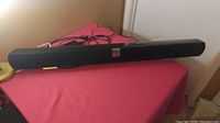 Full view of black Vizio sound bar placed on a pink surface. Shows the entire length and attached cables.