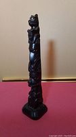 Front side view of the carved totem pole showing stacked figures and smooth polished dark wood surface.