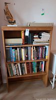 Front view of the vintage wood bookcase filled with books and a decorative sailboat on top.