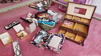 Overview photo showing multiple open and closed jewelry boxes filled with assorted costume jewelry such as clip on earrings, necklaces, rings, brooches, bracelets, pins, and other small items scattered around.