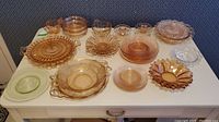 Overhead view of the collection of pink and clear depression glass dishes on a white table showing varying patterns and shapes including round plates, bowls, and handled serving pieces.