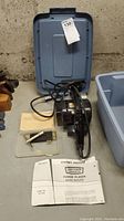 Power planer with power cord, blue carrying case lid, owner's manual, and small accessories box on concrete floor.