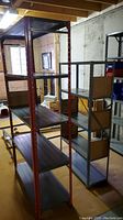 View of two metal shelving units in basement showing red shelving unit on left and gray shelving unit with pegboard sides on right
