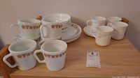 Photo of a collection of ceramic mugs and plates including tan and brown floral pattern mugs and white plates.