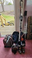 Full kit against door, showing skis, boots, helmet, goggles and carrying bag