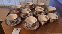 Overview photo showing eight tea cups and saucers arranged on wooden table.