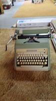 Full view of the green Smith Corona manual typewriter placed on carpet with visible carriage return lever and keyboard.