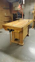 Three-quarter view of bench showing butcher-block top, front vise and leg assembly