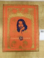 Slipcase closed showing red-orange cloth with gilt embossed border and portrait of George Harrison, title on front