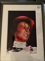 Framed color photographic print showing David Bowie in Ziggy Stardust makeup and costume, front view with white mat and black frame
