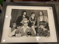 Framed black-and-white photo showing full composition of six celebrities behind glass