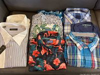 Six folded shirts showing two dress shirts, two printed shirts and two plaid button-downs