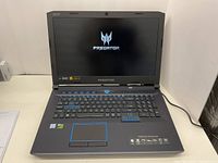 Laptop powered on showing Predator logo on display, blue backlit keyboard visible