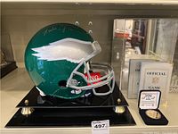 Signed green Philadelphia Eagles helmet on black display stand with silver facemask and coins visible at right