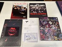 Overview of autographed card in plastic sleeve, certificate, Bill Wyman book, two documentary releases and black lips hardcover book