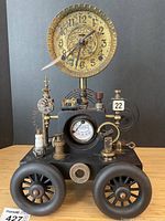 Full front view showing ornate brass clock dial atop black metal base with four cast wheels and industrial parts