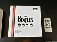 Closed white outer sleeve with The Beatles logo, Montblanc branding and rainbow stripe detail.