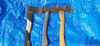 Three used hatchets on blue tarp, showing handles and heads