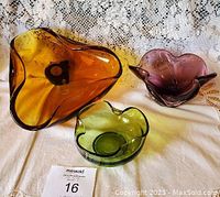 Photo of three vintage glass bowls: large amber, medium amethyst, small green on white cloth with lace background.