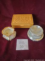 Photo of the three music boxes on a dark red background including a rectangular wooden box, an octagonal porcelain box without lid, and a round metal box without lid, shown from the top.