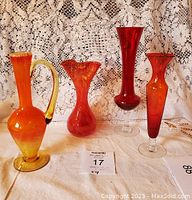 Four amberine glass pieces displayed on a lace tablecloth showing range of colors and shapes.