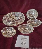 Five crystal ashtrays arranged on a burgundy backdrop with a lot card showing number 49, showing different sizes and cut designs.