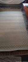 Showing full view of the beige area carpet with embossed pattern on the floor near a sofa and wooden table.