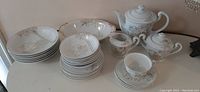 Full view of set items including plates, teacups, teapot, sugar bowl, and pitcher on white surface.