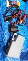 Jumper cables, battery charger, and a container of wipes on a blue tarp