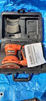 Black & Decker palm sander inside molded black plastic carrying case with instruction manual visible.