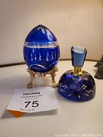 Photo showing cobalt blue crystal egg on gold-tone stand alongside blue crystal perfume bottle