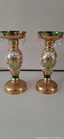 Pair of green glass candle lusters with gold and white handpainted decoration, crystal rings on ribs, shown side by side.