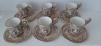 Six porcelain demitasse cups and saucers arranged in two rows, showing full set and detail of design and color