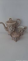 Full view of Capodimonte teapot, sugar bowl, and creamer showing cherub relief and gold accents.