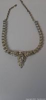 Full length view of silver-tone laurel leaf motif necklace with artichoke-shaped centerpiece pendant against a white background