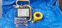 Full view of industrial halogen work light, three packages of halogen bulbs, and caution tape on blue tarp.