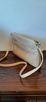 Side view of the cream leather shoulder bag with an adjustable strap showing the design and texture of the bag.