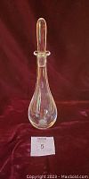 Full view of the Orrefors crystal decanter with stopper against red background, showing shape and clarity.