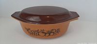 Side view of orange Pyrex Old Orchard casserole dish with brown lid and fruit pattern design.