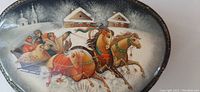 Full view of oval Russian lacquer box lid showing detailed hand-painted winter troika scene with three horses pulling a sleigh carrying people, snow-covered houses in background.
