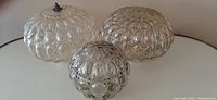 Set of 3 antique bubble glass light shades, 2 large and 1 small, placed on a white surface showing the bubble textured surface and smokey grey color.