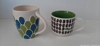 Two 2009 Starbucks ceramic mugs, tall with blue and green scale design and shorter with coffee bean pattern and green interior.