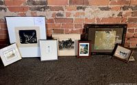 Full view of all seven framed artworks leaning against an exposed brick wall, showing size and variety.
